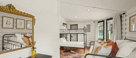 Ein Schlafzimmer mit Etagenbett, einem Einzelbett, einem Spiegel mit Zierrahmen, einer Kommode und einem Kuhfellteppich.