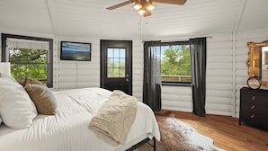 Un dormitorio con cama, ventilador de techo, televisión, cómoda y ventana con cortinas.