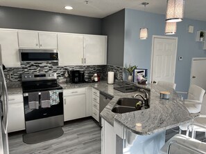 A modern kitchen with white cabinets, a stainless steel stove, a microwave, and a granite countertop.