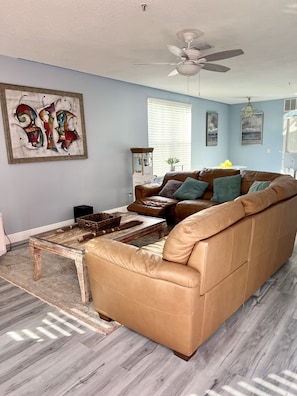 A living room with a brown leather sofa, a wooden coffee table, and a ceiling fan.