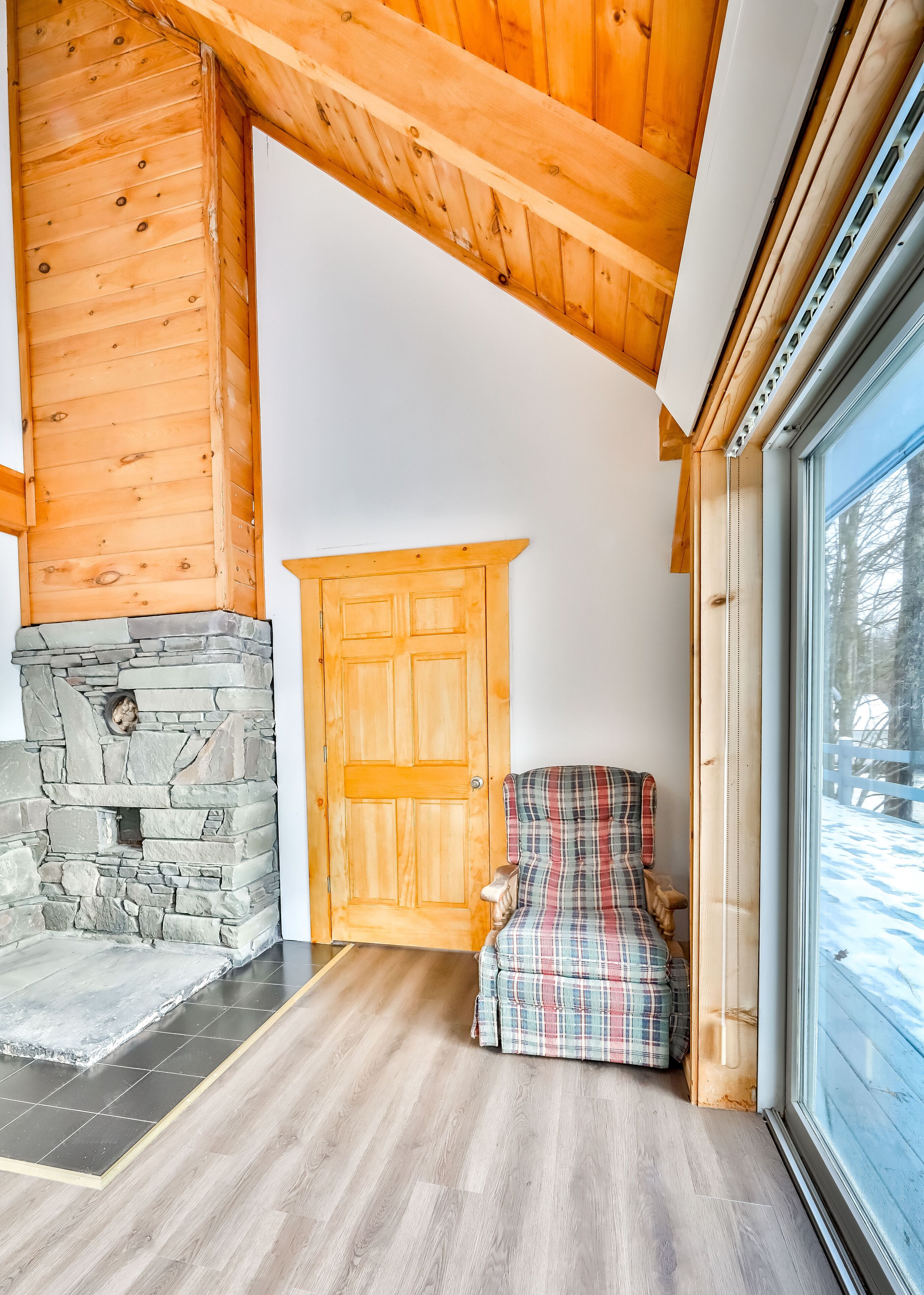 A cozy room with a stone fireplace, a plaid armchair, and a wooden door.