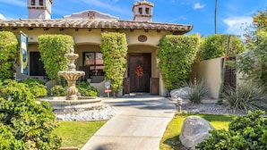 A Mediterranean-style house with a stone pathway leading to a wooden door, surrounded by lush greenery and a stone fountain. - SPANISH TRADITIONAL - MOVIE COLONY EAST;  PS City ID #038084 (Palm Springs)