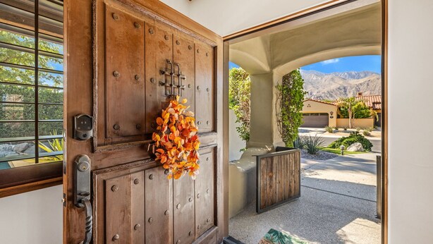 A wooden door with a keyhole and a lock, a small window with metal bars, and a view of a mountain landscape through an archway. - SPANISH TRADITIONAL - MOVIE COLONY EAST;  PS City ID #038084 (Palm Springs)