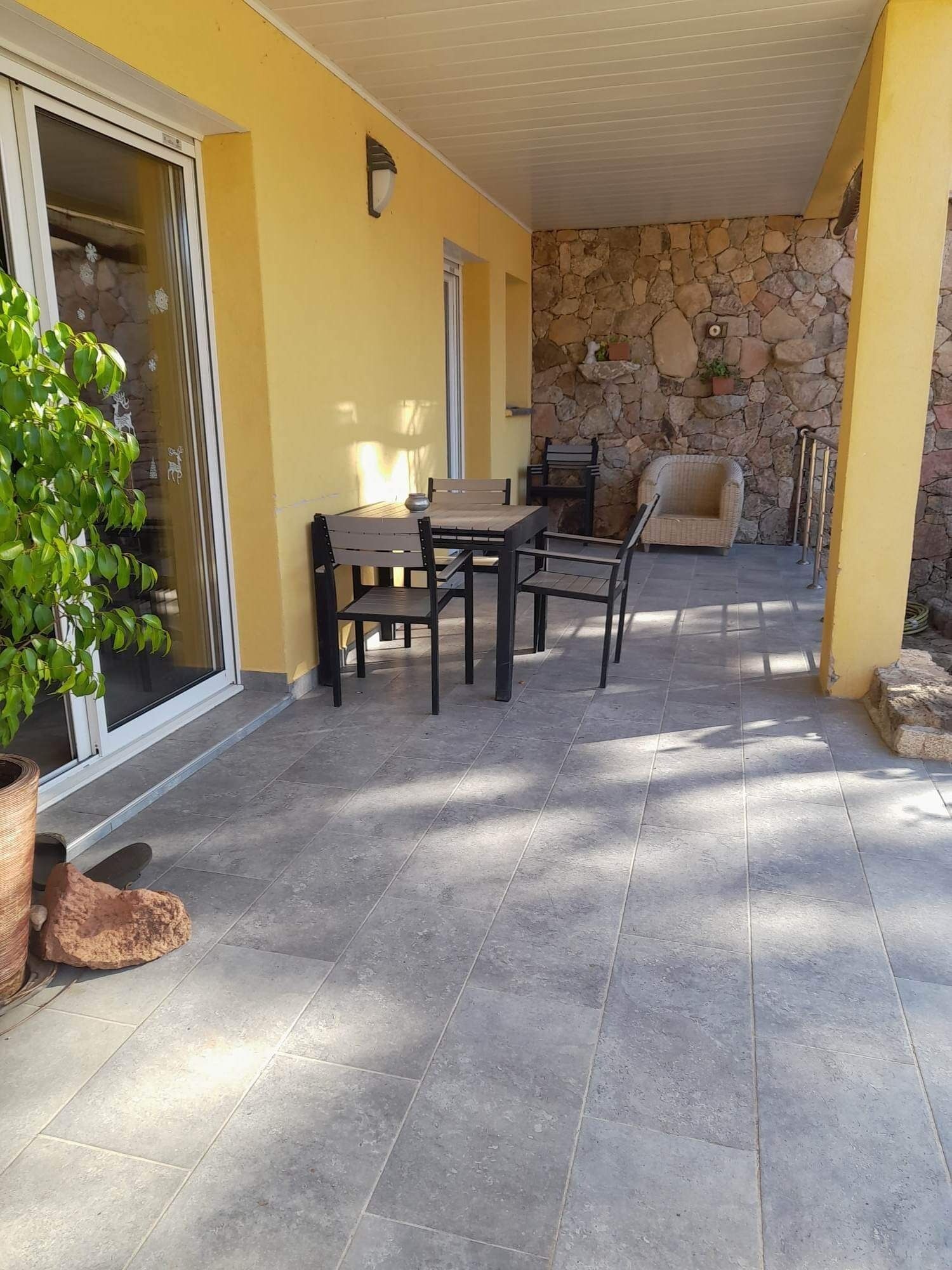 A covered patio area with a stone wall, a table with chairs, and a wicker chair.