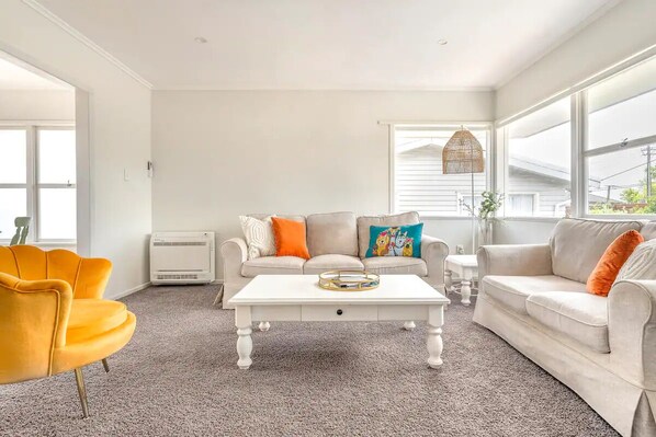 A living room with a white sofa, a yellow armchair, and a white coffee table. - Bright & Central Home with Mini Golf Area (Auckland)
