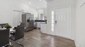 Una cocina moderna con armarios blancos, electrodomésticos de acero inoxidable y un comedor con mesa y sillas.