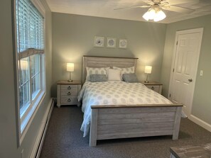 A bedroom with a bed, two bedside tables, a ceiling fan, and a door.