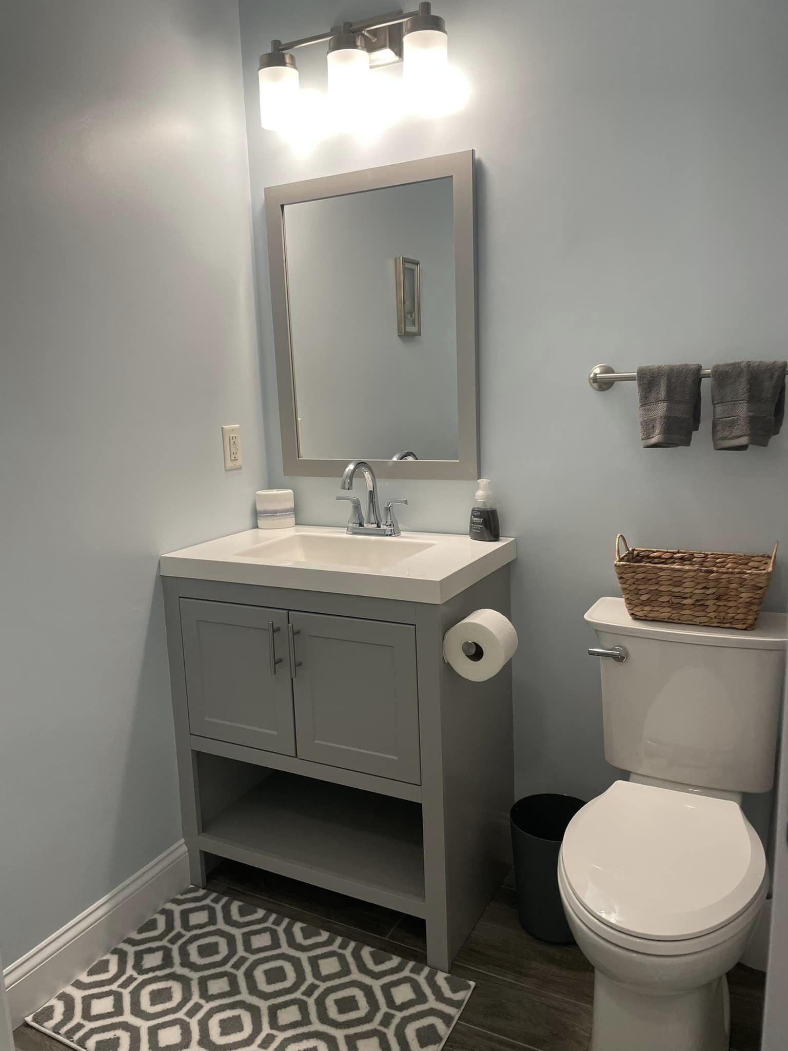 A bathroom with a grey vanity, a mirror, a toilet, and a patterned rug.