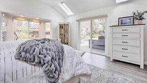 A bedroom with a large bed, a ceiling fan, a skylight, a white dresser, and a view of the outdoors. - Peaceful Windsor Retreat w/ Private Hot Tub! (Windsor)