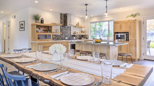 A modern kitchen with wooden cabinets, a central island, and a dining area set up for a meal. - Peaceful Windsor Retreat w/ Private Hot Tub! (Windsor)