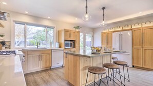 A modern kitchen with wooden cabinets, a central island with stools, a microwave, and a refrigerator. - Peaceful Windsor Retreat w/ Private Hot Tub! (Windsor)