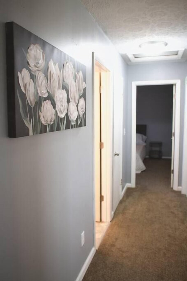 Ein Flur mit einem Gemälde von weißen Tulpen an der Wand, Teppichboden und einer Tür zu einem anderen Raum.
