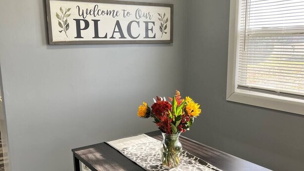A welcome sign, a vase with flowers, and a table with a lace table runner. - 600 House (West Lafayette)