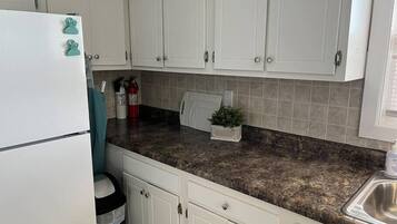A kitchen with white cabinets, a granite countertop, a stainless steel sink, a refrigerator, and a fire extinguisher.