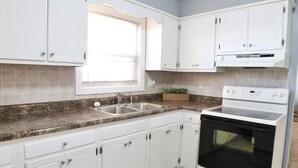 A kitchen with white cabinets, a double sink, a built-in oven, and a window with blinds. - 600 House (West Lafayette)