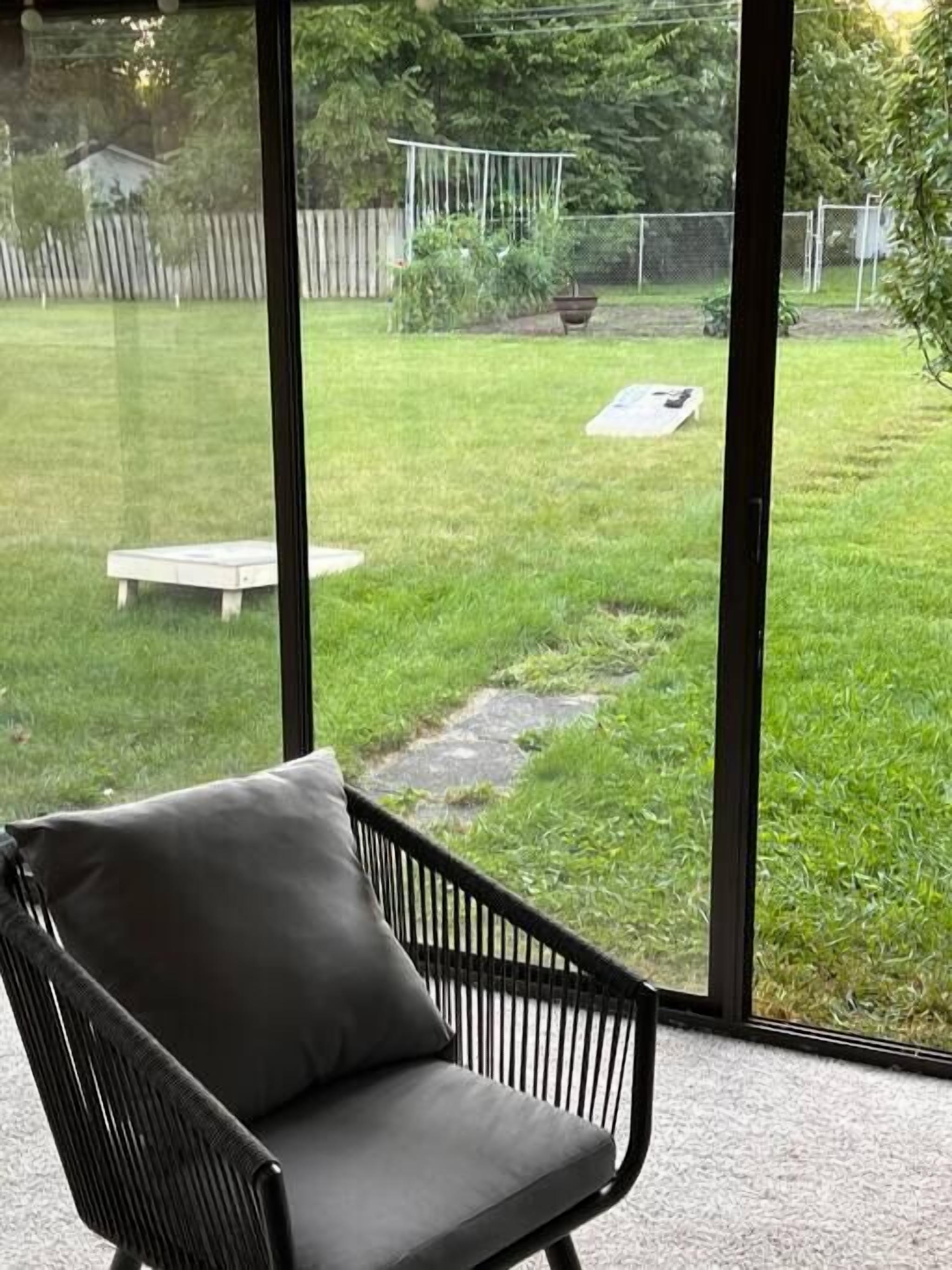 Une pièce dotée d’une grande fenêtre donnant sur une cour arrière aménagée avec une terrasse en bois, un banc et un jardin.