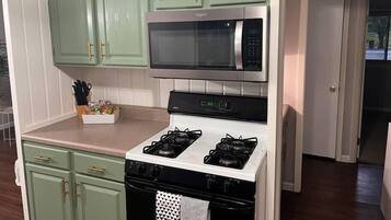 Una cocina con gabinetes verdes, microondas, estufa y lavamanos.