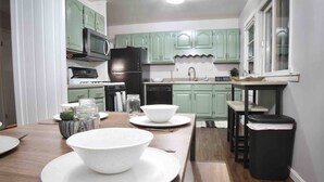 A compact kitchen with green cabinets, a black refrigerator, and a wooden dining table set with white plates and bowls. - Salisbury (West Lafayette)