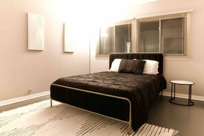 A bedroom with a bed, a round side table, and a window with blinds. - Salisbury (West Lafayette)
