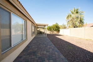 A covered patio area with a brick floor, large windows, and a palm tree in the background. - Charming 4 Bedroom, 2 Bathroom house in Phoenix (Phoenix)