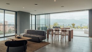 A spacious living room with a grey sofa, wooden dining table, and chairs, large windows offering a city view. - View of Medellin - Private Terrace & Hot Tub - AC - Deluxe - Wake 1311 (Medellín)