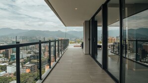 A modern balcony with a glass railing, offering a cityscape view with mountains in the distance. - View of Medellin - Private Terrace & Hot Tub - AC - Deluxe - Wake 1311 (Medellín)