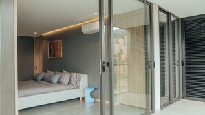 A modern room with a glass door leading to an outdoor area, a sofa with cushions, a small blue side table, and a wall-mounted air conditioner. - View of Medellin - Private Terrace & Hot Tub - AC - Deluxe - Wake 1311 (Medellín)