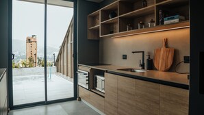 A modern kitchen with a large window, wooden cabinets, and a built-in shelf with kitchen items. - View of Medellin - Private Terrace & Hot Tub - AC - Deluxe - Wake 1311 (Medellín)