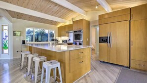 Una cucina moderna con mobili in legno, un'isola centrale con sgabelli, elettrodomestici in acciaio inossidabile e un'ampia finestra che offre luce naturale.