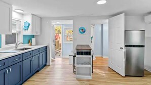 A modern kitchen with dark blue cabinets, a stainless steel refrigerator, and a wooden floor. - Cottage by the Sea (Warwick)
