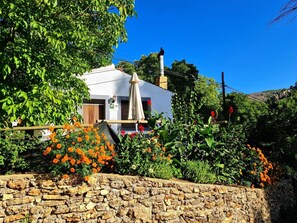 Un muro de piedra con un edificio blanco al fondo, rodeado de follaje y flores naranjas.