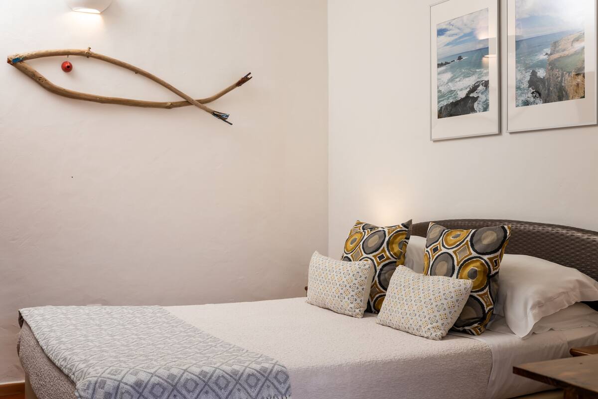 A neatly made bed with patterned bedding, a branch decoration with a red ornament, and two framed pictures on the wall.