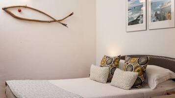A neatly made bed with patterned bedding, a branch decoration with a red ornament, and two framed pictures on the wall.