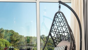 Una silla colgante con cojín y un tapete tejido en una habitación con un ventanal y vistas al verdor.