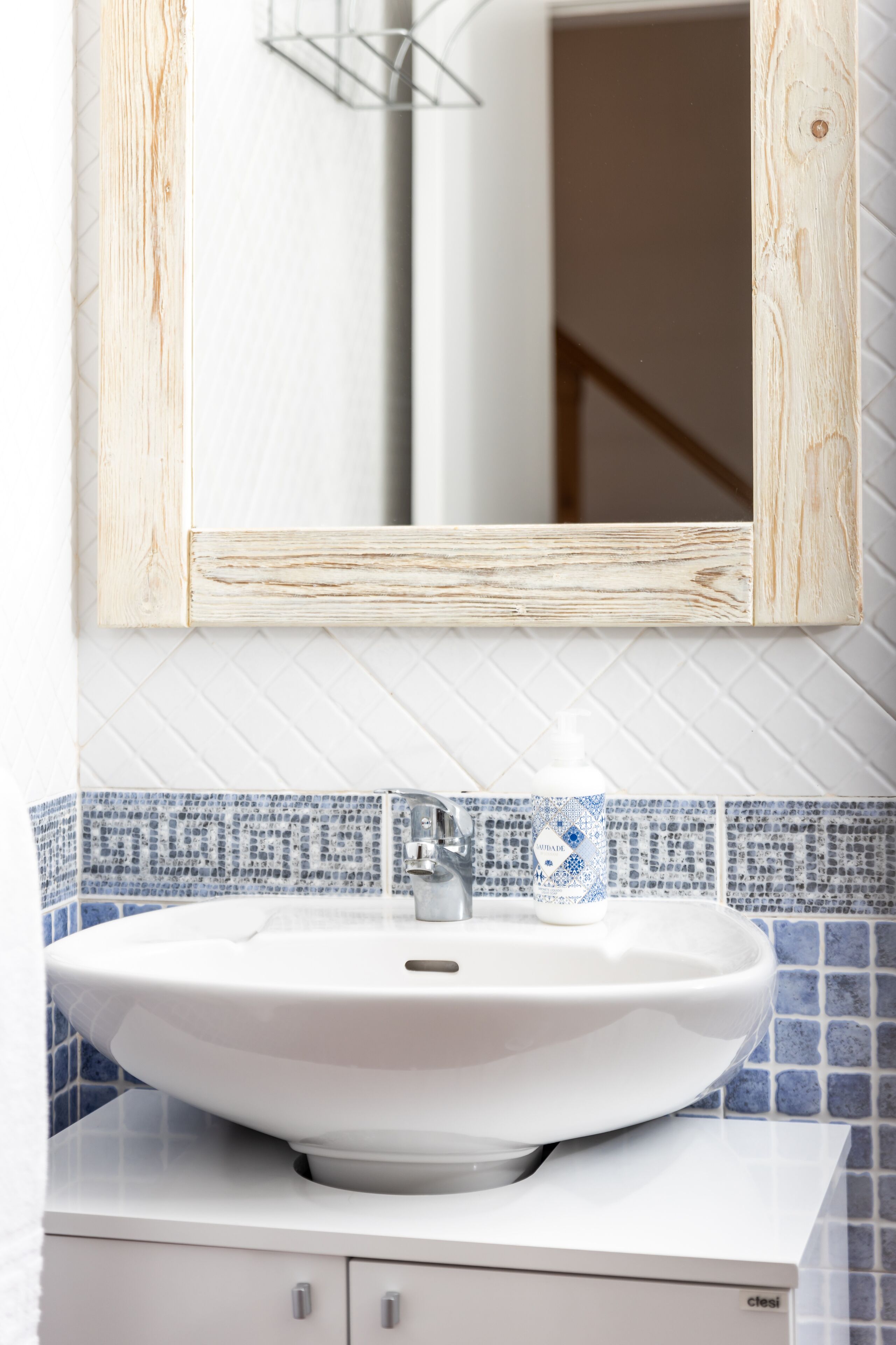Een badkamer met een witte wastafel, een spiegel met houten lijst en blauw-witte betegeling.