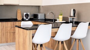 Una cocina moderna con armarios de madera, encimera negra, una isla de madera y tres sillas blancas.