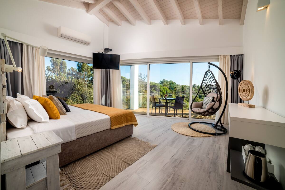 A modern bedroom with a large bed, a hanging chair, and a view of the outdoors.