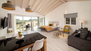 Una habitación amplia con una cama, un sofá, un rincón de comedor y un ventanal con vistas al exterior.
