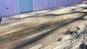 Un edificio rosa con una terraza de madera, una puerta blanca y dos ventanas.