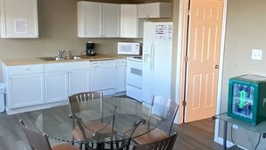 Cocina compacta con armarios blancos, un microondas, un refrigerador y una mesa de vidrio con cuatro sillas.