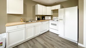 Una cocina con gabinetes blancos, microondas, estufa y refrigerador.