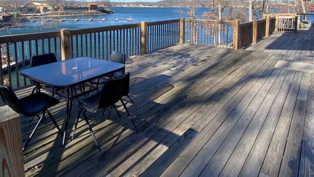 Una terraza de madera con una mesa y sillas, con vista a un cuerpo de agua.