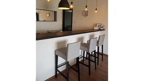 Zona de bar con una barra alargada, cuatro taburetes, iluminación colgante y un espejo sobre la barra.