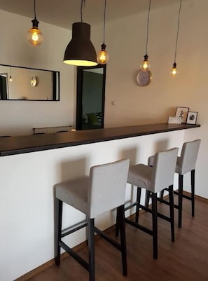 A bar area with a long counter, four bar stools, pendant lighting, and a mirror above the counter.