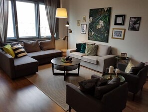 Ein modernes Wohnzimmer mit zwei Sofas, einem Couchtisch und einem Beistelltisch mit Kerzen. An den Wänden befinden sich gerahmte Bilder und über dem Sofa ein großes Gemälde.