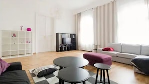 A modern living room with a sofa, two round tables, a TV, and a bookshelf. - Downtown Rising Sun (104sqm 2bedr/2bath/living) (Budapest)