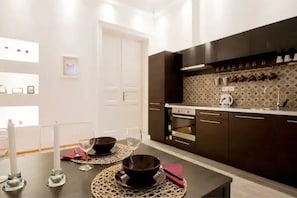 A modern kitchen with dark cabinets, a countertop, and a backsplash. There is a dining table with a placemat, a candle, and a wine glass.
