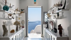 A hallway with white shelves displaying various sculptures and vases, leading to a door with a view of the sea. - Oia Treasures Art Suites (Santorini)