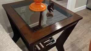 A glass-top table with a wooden frame, a lamp with an orange base and a white lampshade, and a small horse figurine. - Stylish and cozy 2 bed (Brighton)