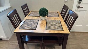 A wooden dining table with four chairs, a small potted plant, and woven placemats. - Stylish and cozy 2 bed (Brighton)